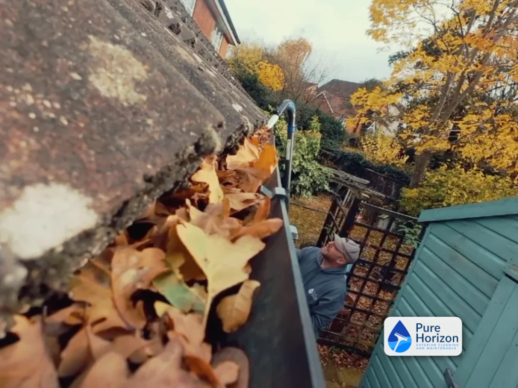 Autumn gutter clearing with fallen leaves packed inside a roofline gutter