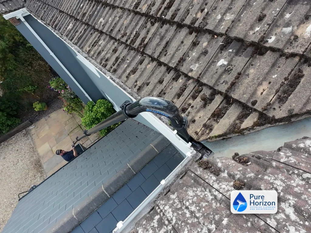 High-reach gutter-vacuum pole extending over a lower pitched roof to clear an inaccessible gutter
